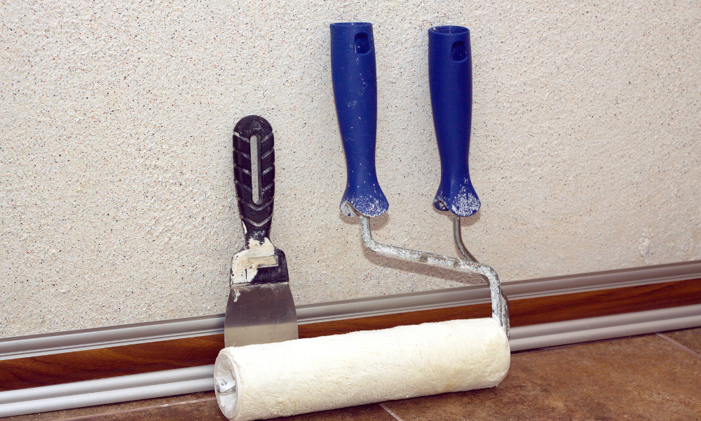 Paint rollesr and trowel stands in a room at baseboard